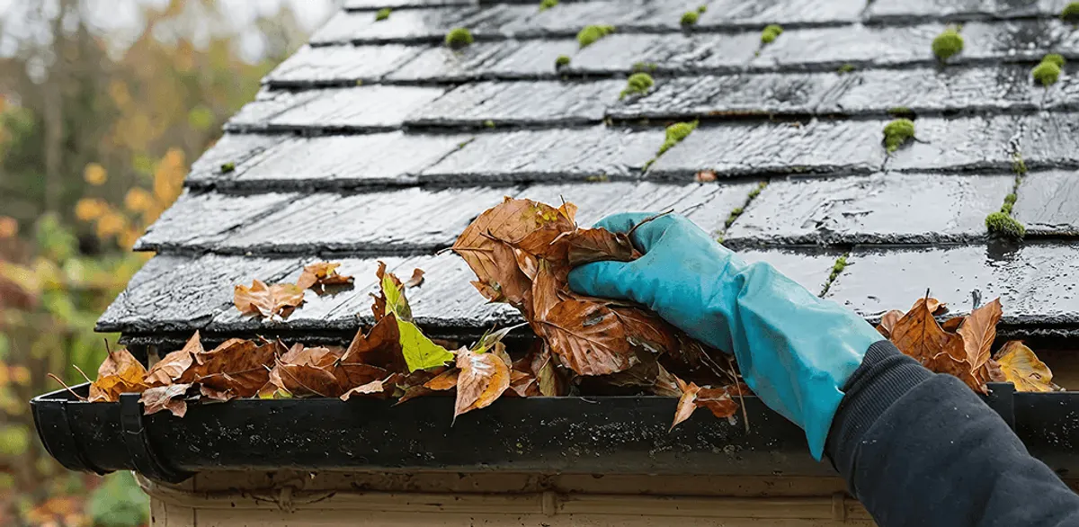 Gutter cleaning technician clearing wet leaves from roof gutters in Spokane, WA